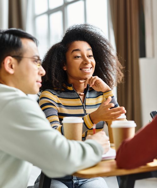 A multicultural group of students, including Caucasian, Asian, and African American members, engaged in discussion at a table.